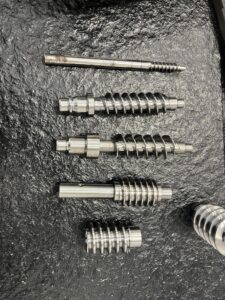 A display of several complex metal parts machined with high precision by the MX500 whirling machine. These parts feature a high surface finish and intricate details, highlighting the machine's advanced manufacturing capabilities, arranged against a clean, industrial background.