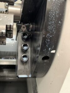 A close-up view of the tool holder assembly on a PH46-750 CNC Whirling Machine. The image shows a precision-mounted carbide insert secured by hex-head bolts on the rotating cutter head, coated with white coolant emulsion.