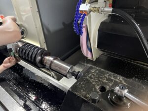 An operator works with hands near a large worm gear workpiece on the SMK1507 CNC Thread Grinding Machine, which is held between centers. The base is covered in coolant, and the grinding wheel is visible to the right.