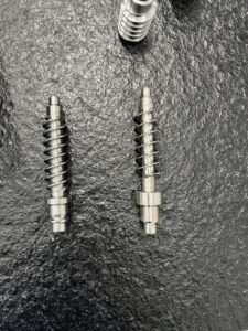 An overhead close-up view of two shiny, high-precision-ground worm gear samples resting on a textured black surface, showcasing the surface finish achievable by the SMK1507 CNC Thread Grinding Machine.